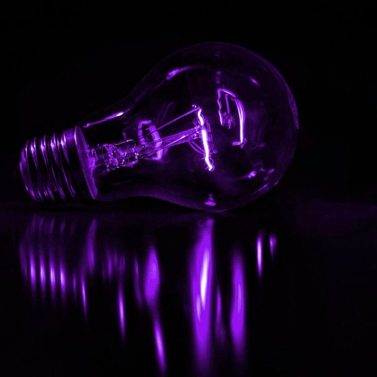 Ampoule à filament émettant une lumière violette sur fond sombre.